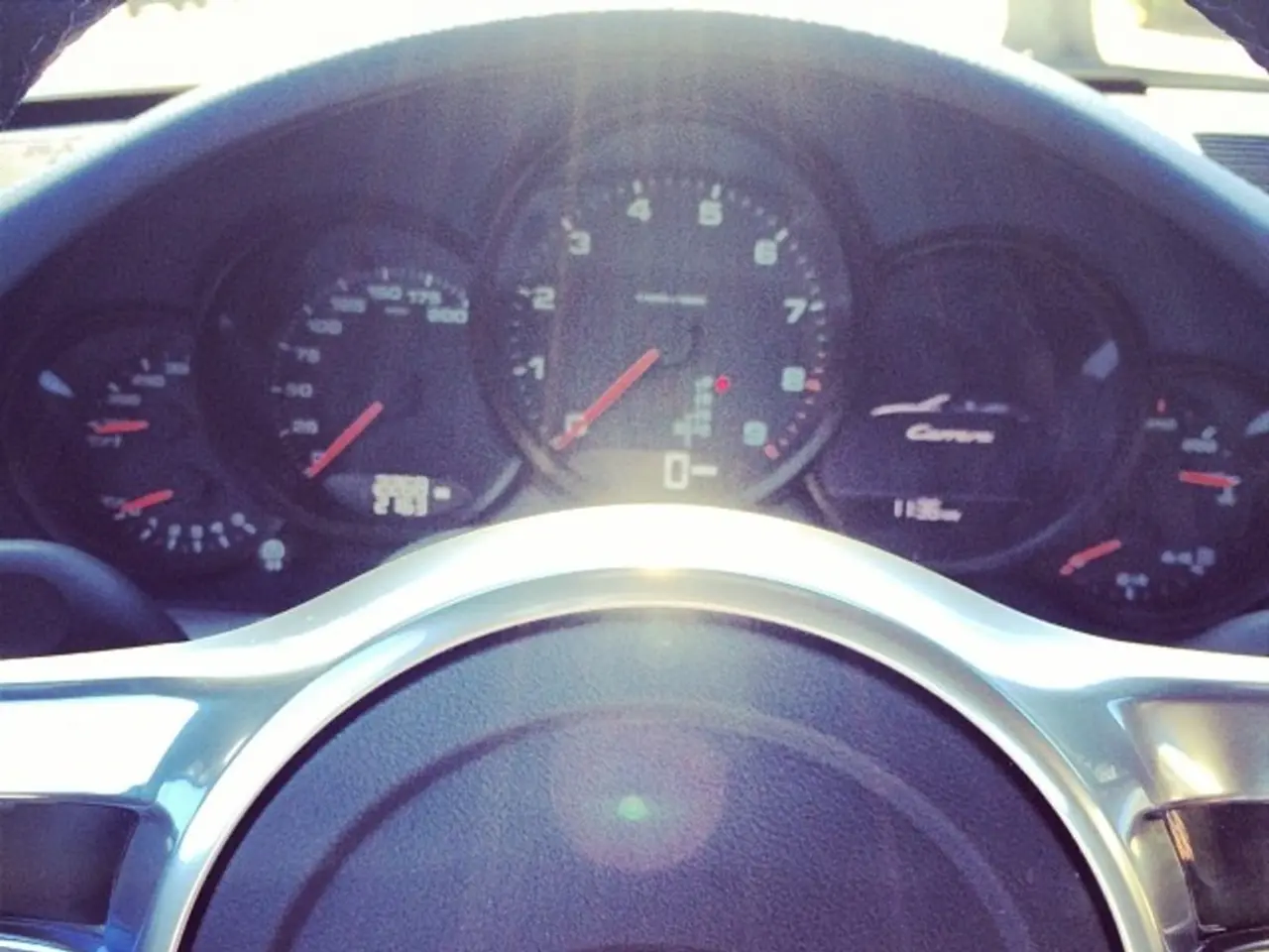 In this image we can see the speedometer and steering of the Porsche car.