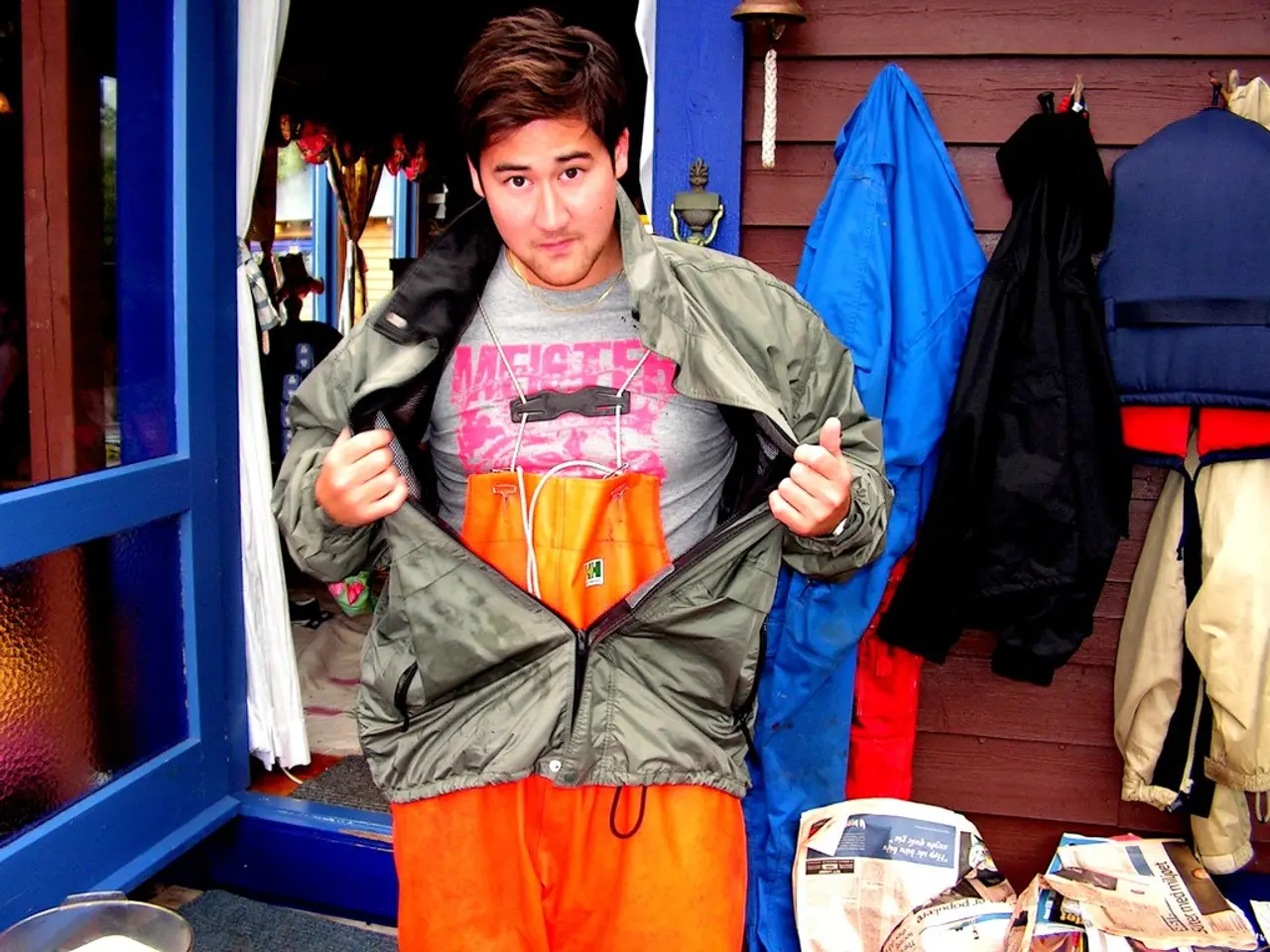 In this image, in the middle there is a jacket, t shirt. In the background there are jackets,...