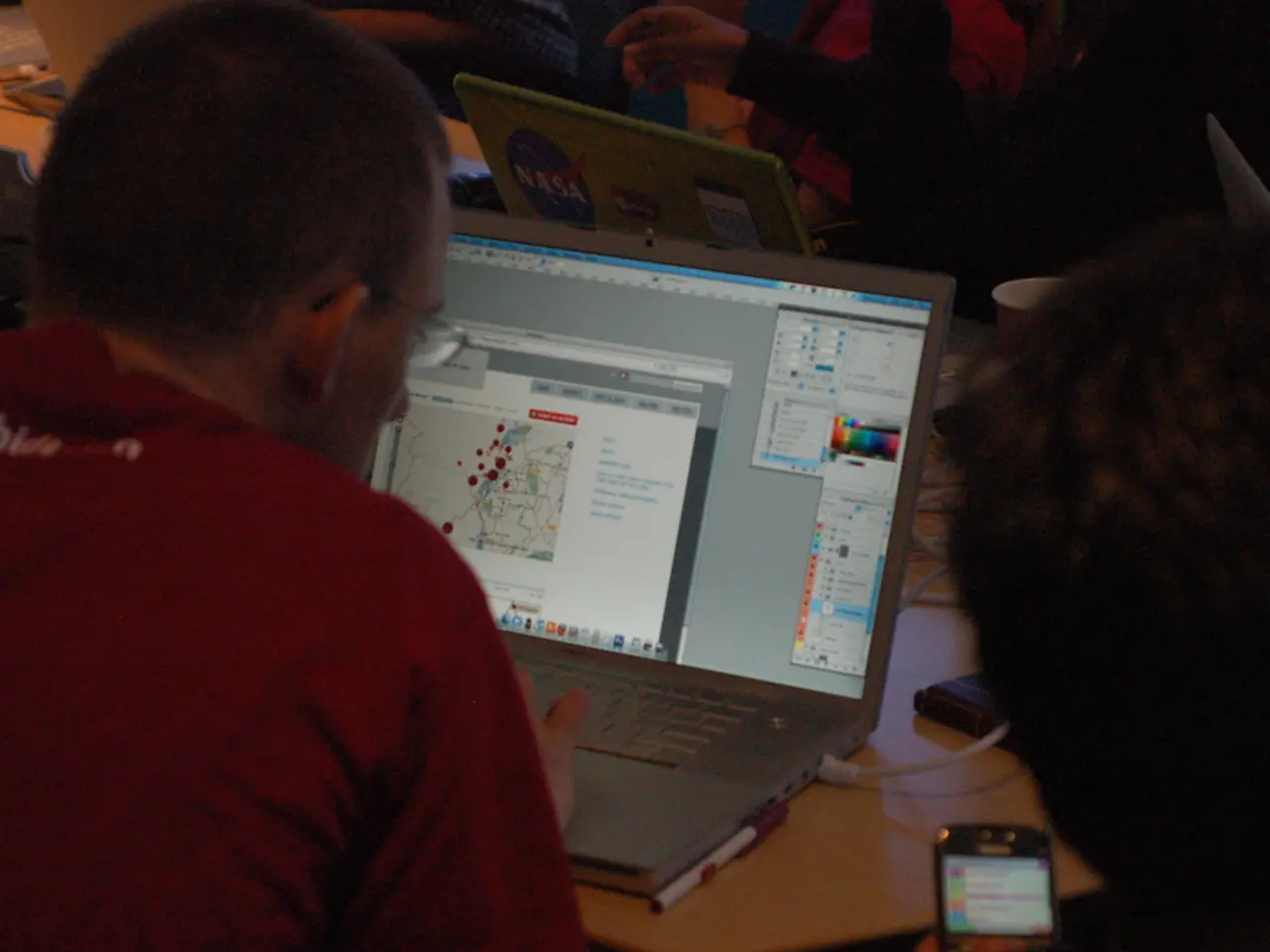 In this image we can see a few people around the table using laptops, there we can see a person...