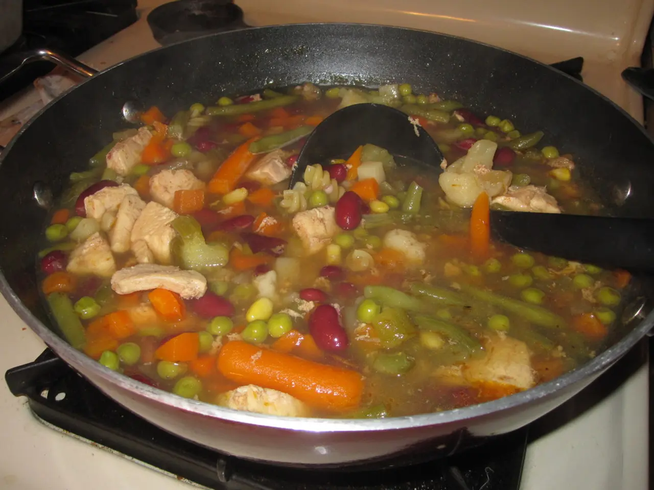 In this picture, we see the pan containing vegetables, water and spoon are placed on the gas stove.