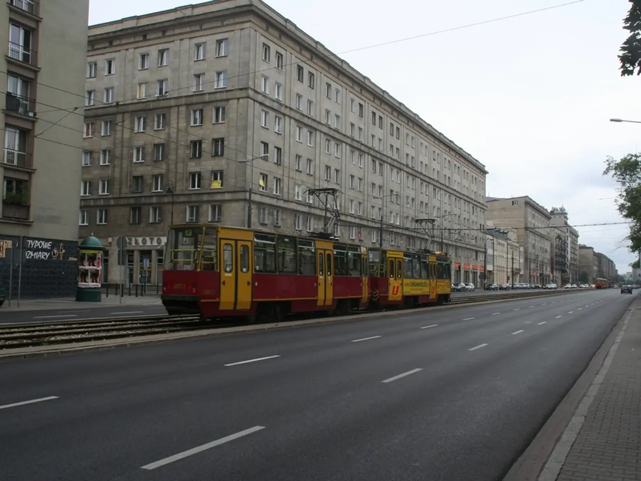 In this image, in the middle there are buildings, vehicles, train, street lights, poles, cables,...
