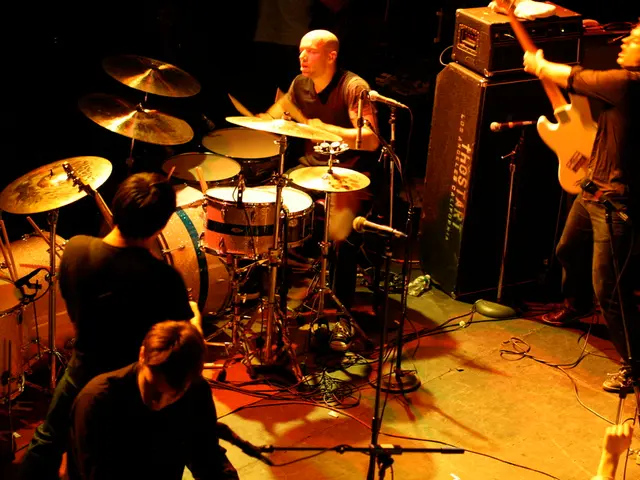 The image is inside the room. In the image there are two people playing their musical instruments,...