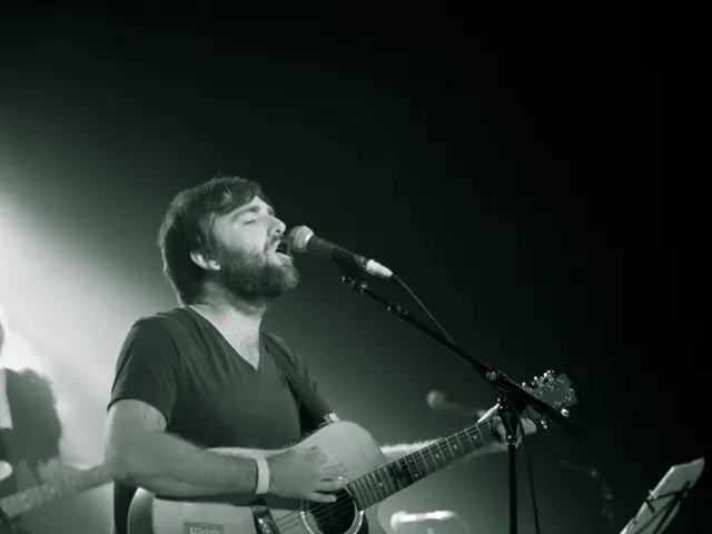 In the picture we can see a man standing and holding a guitar and singing a song in the microphone....