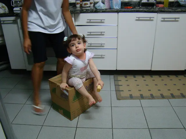 In this picture we can see a girl holding object in her hand and sitting on a box. There is a...