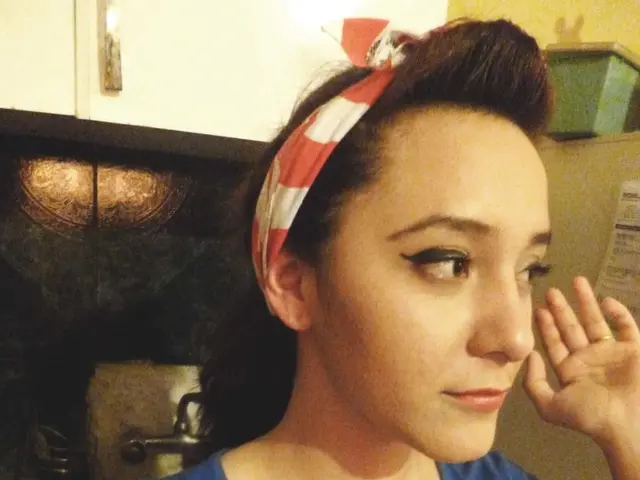 In the image there is a woman in blue t-shirt and red hair band standing in front of table, it...