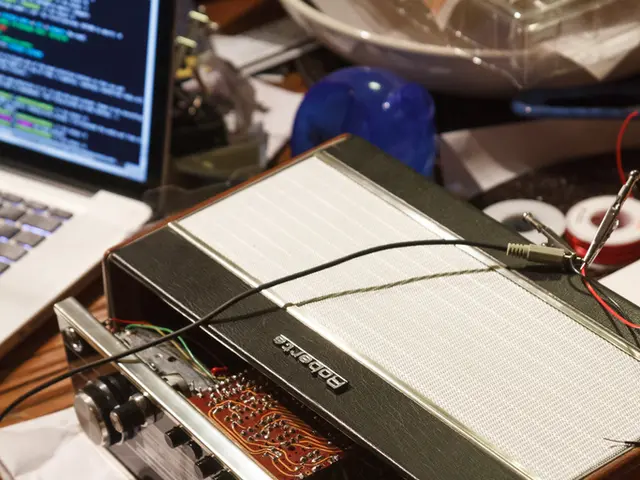 On a wooden table we can see a laptop, tapes, an electronic device, cutting plier, wires and few...