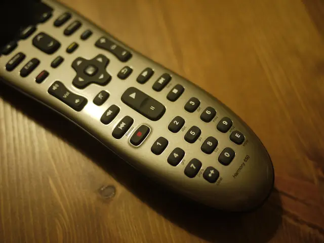 In this image there is a remote on a wooden surface. There are numbers, text and symbols on the...