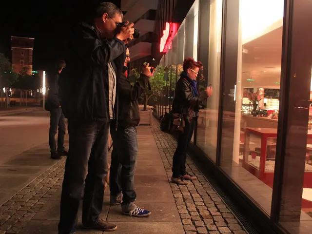 In the image I can see people holding the cameras and to the side there is a glass from which I can...